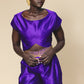 Woman wearing a purple outfit with gold accents against a beige background