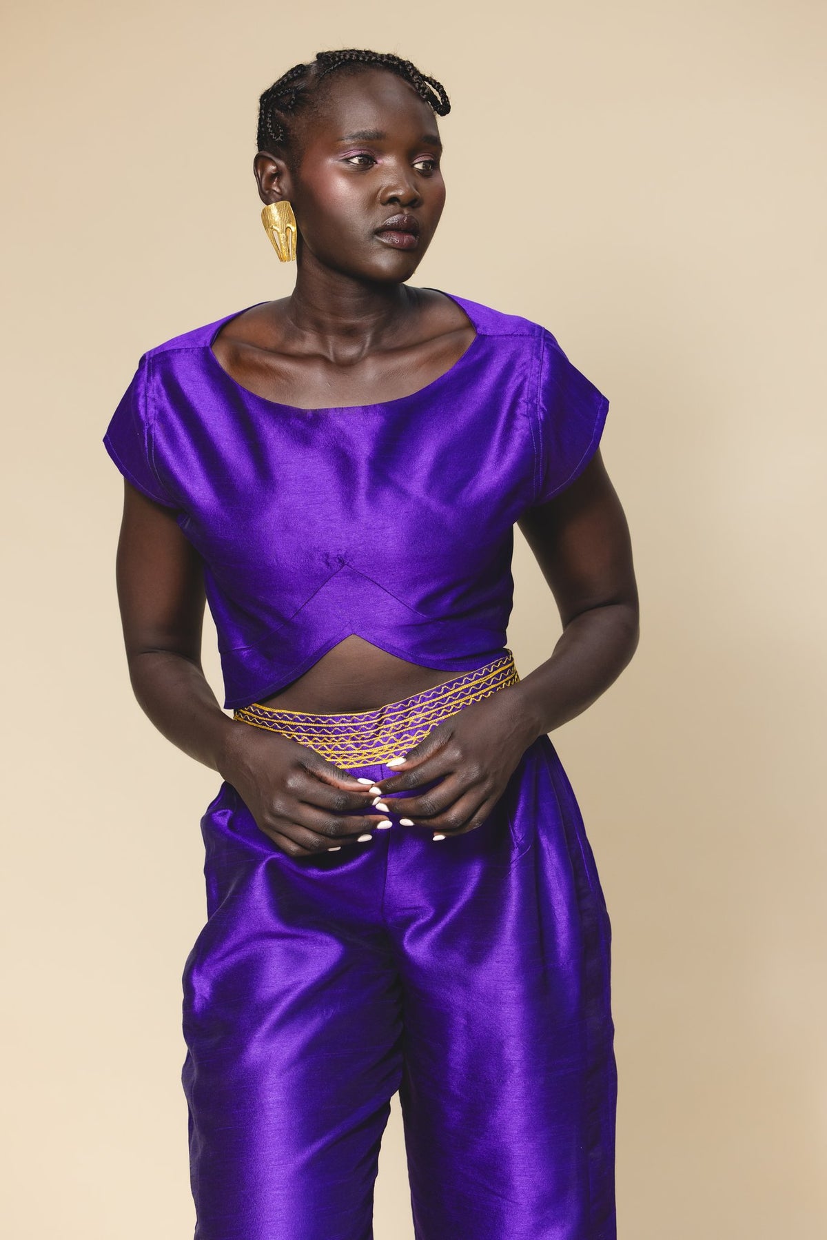 Woman wearing a purple outfit with gold accents against a beige background