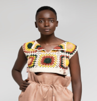 A model wearing a sleeveless crochet crop top with a multicolor granny square pattern and matching high-waisted peach shorts, set against a plain light gray studio background.