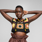 A model posing in a black crochet crop top with colorful sunflower patterns and brown paperbag shorts against a light gray studio background.