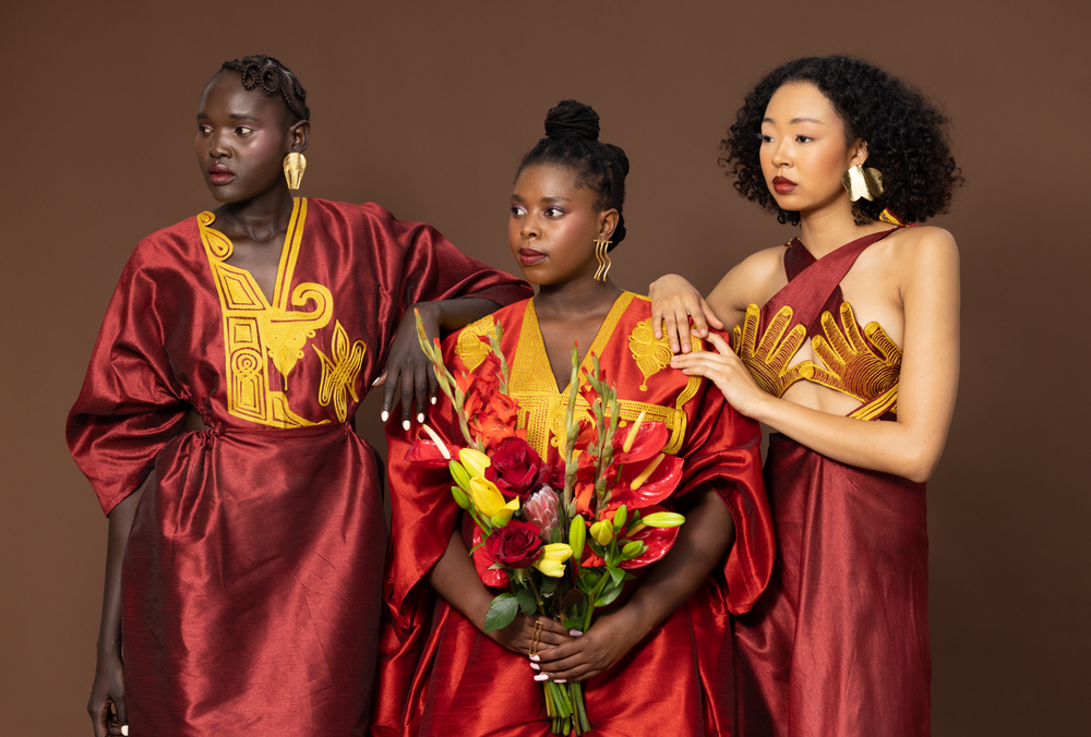 Three women in red and gold traditional outfits against a brown background